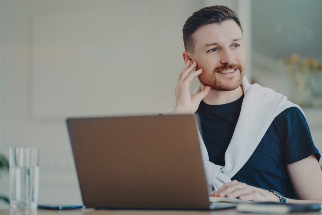 Cheerul man working remotely on laptop at home, having online meeting