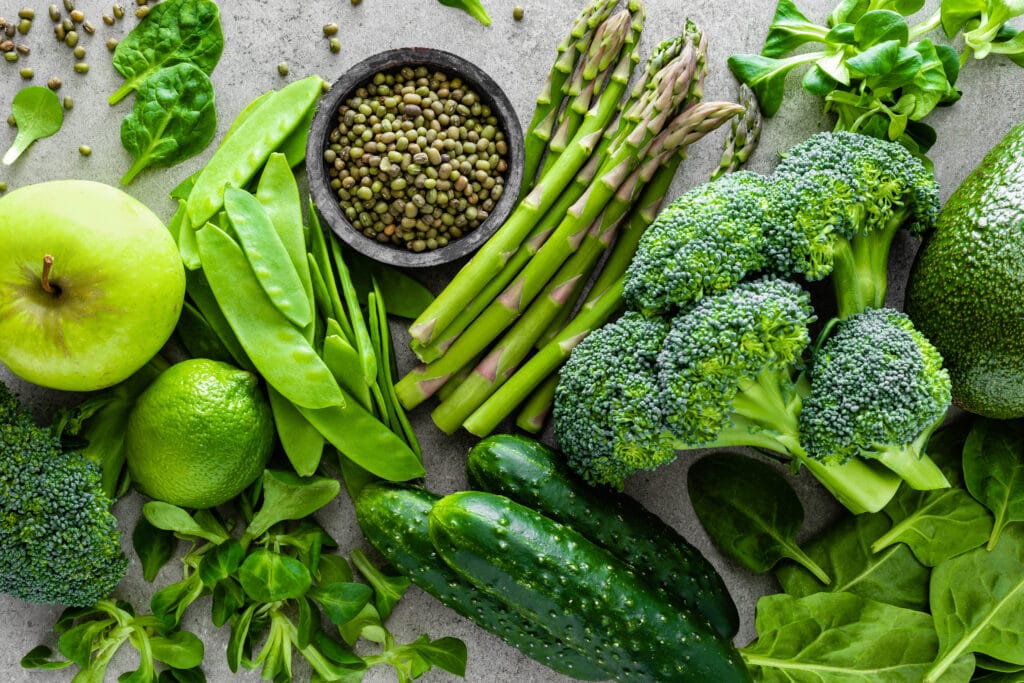 Healthy vegetarian food concept background, fresh green food selection for detox diet, raw broccoli, apple, cucumber, spinach, peas, asparagus, avocado, lime, corn salad and mung bean, view from above, flat lay