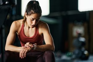 Young athlete checking her heart rate on smart watch during sports training in a gym.